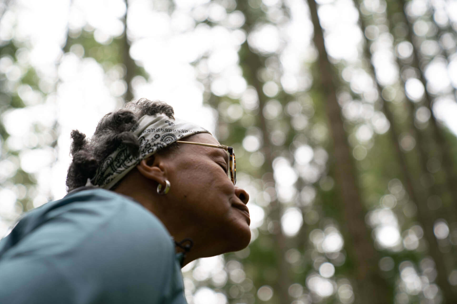 A woman is seen standing in the forest with her eyes closed 