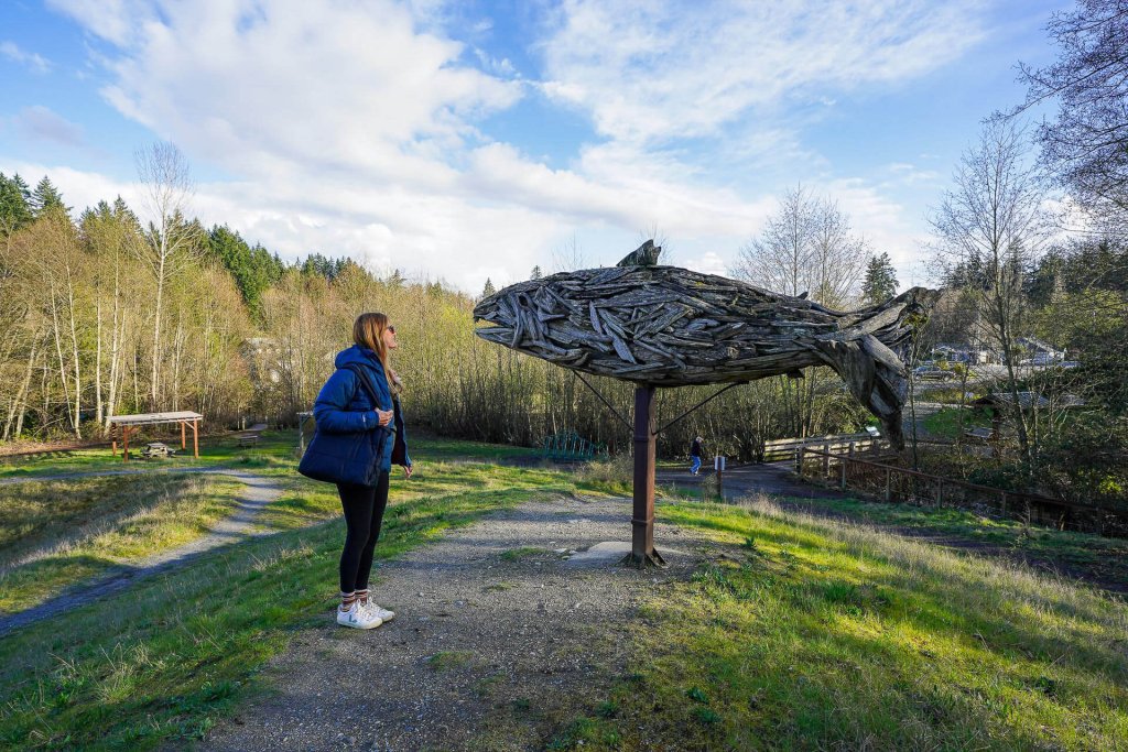 A photo of a woman looking at a sculpture of a fish in a park in Poulsbo