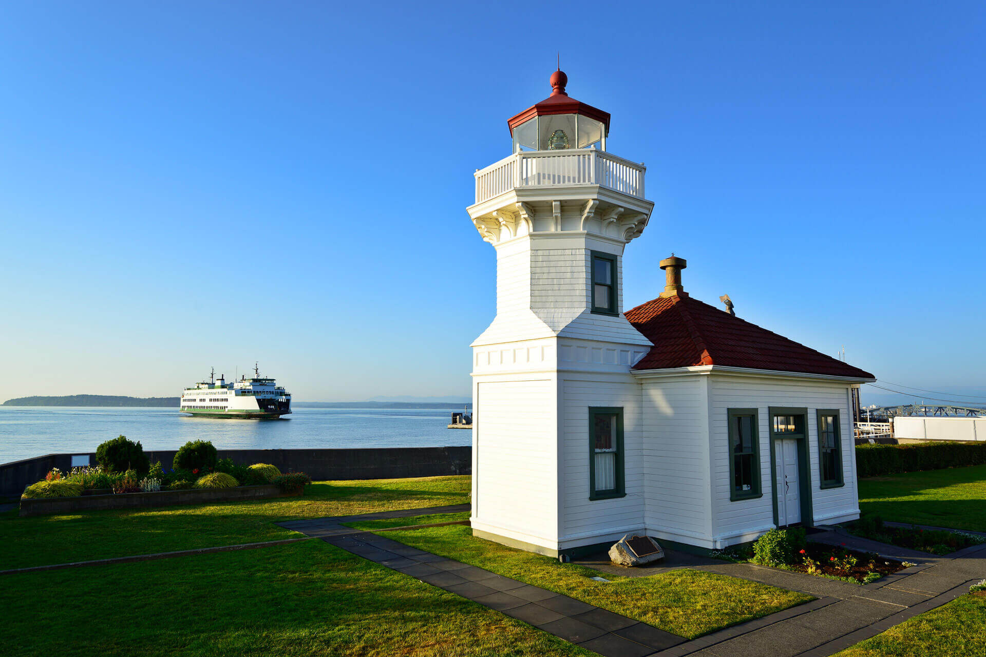 Mukilteo Lighthouse in Washington sits next to the water with a ferry boat in the background.