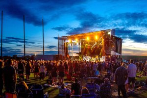 A photo of people standing and sitting on a lawn at sunset as they watch an outdoor concert at Concert Venues in Washington State