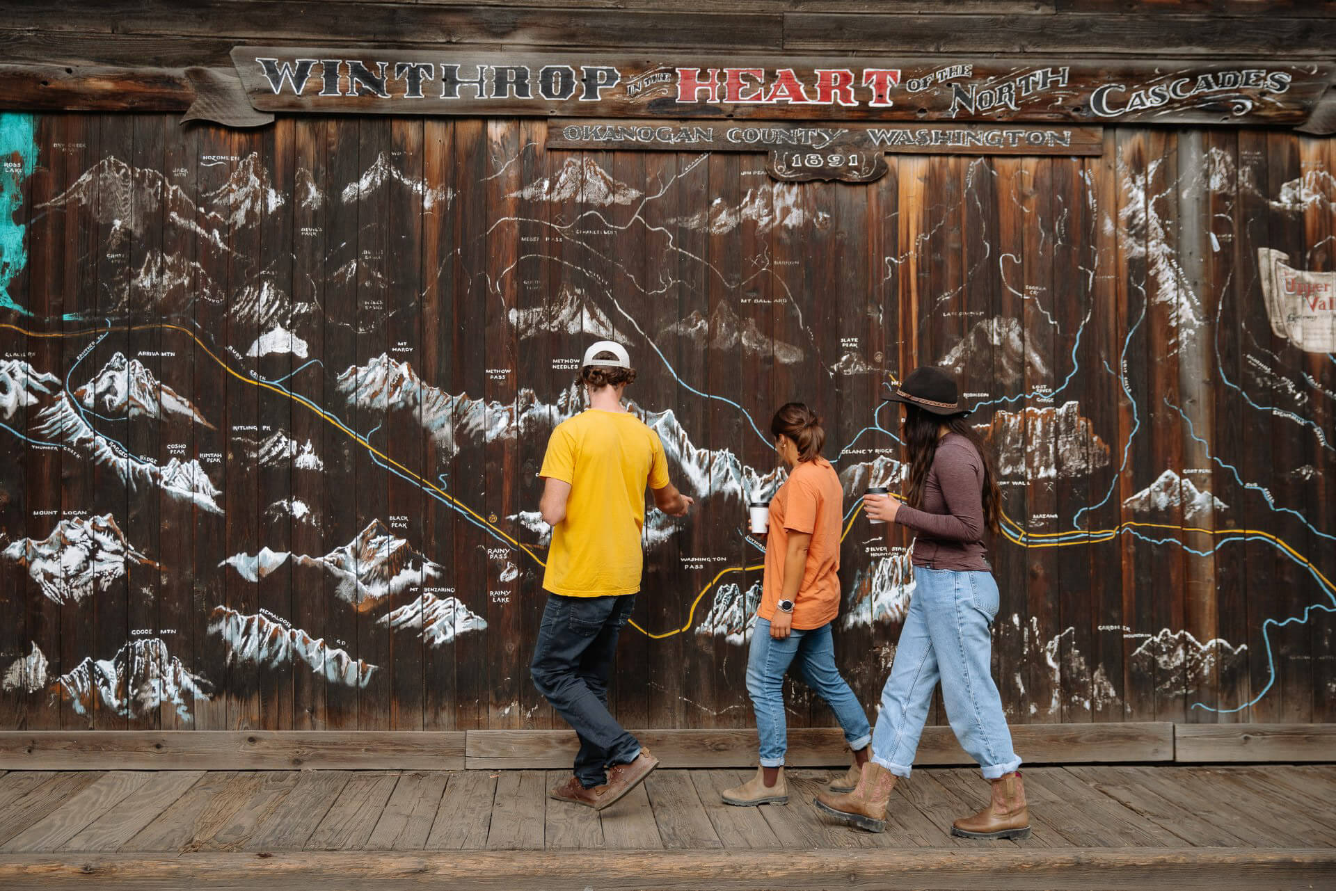 Three people walk past wall with sketches of mountains in Winthrop in the Methow Valley