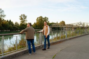 Two men stand on a walking path and look out at the Skagit River.